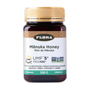A jar of Flora Manuka Honey with labels indicating UMF 5+ and MGO 100+. The jar is set against a white background.